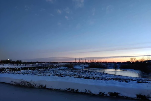 Frozen canal with snow on the side and a distant sunrise
